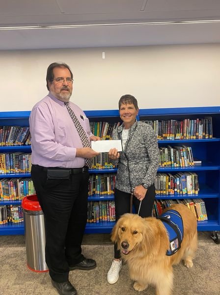 A TOP NOTCH TEACHER, Gina Johannsen has been named Educator Of The Year for the Clinton School District. Pictured with Johannsen is Education Foundation Representative Dan Wallace and school therapy dog, Perry.