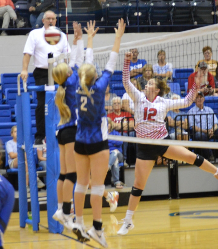 THE LADY CARDS' Braylin Paxton (12) tips the ball past the leaping Kyla Harms in volley action last Tuesday in Cole Camp. Harms and company beat Lincoln in three sets.