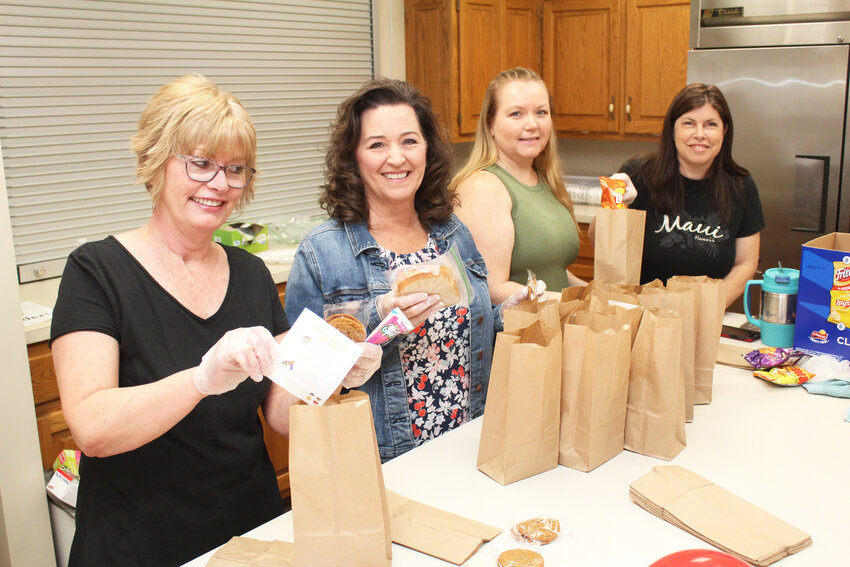 LENDING A HAND, Paula Bullock, Delaina Bullock, Heather Rutter and Kara Manning prepared to hand out free sack lunches that included a sandwich, chips, yogurt, cookie and an invitation to Summer Fun Days at First Baptist Church.