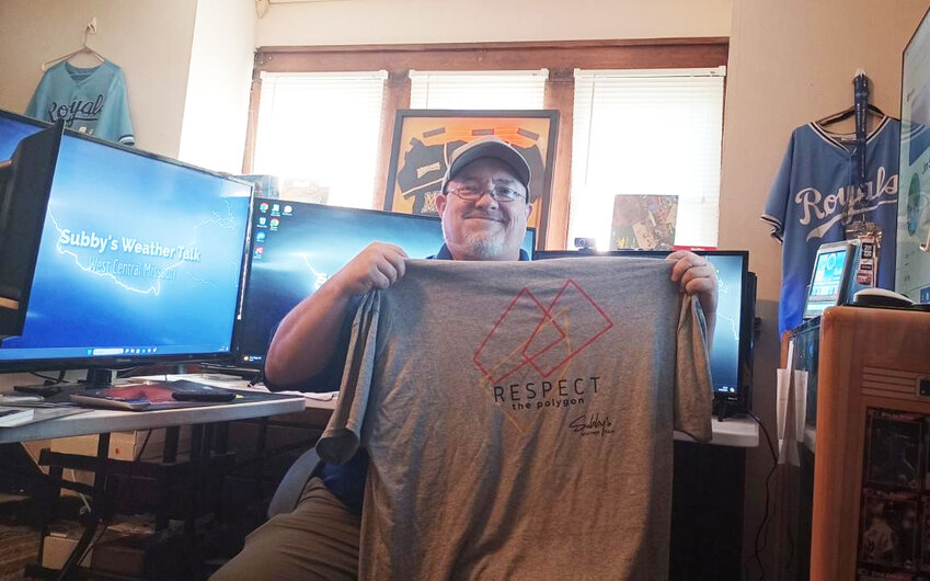 IN HIS WEATHER CENTER, Jim Sublette holds a “Respect the Polygon” T-Shirt. Sublette monitors weather data and disperses information to a wide audience of followers from his live streams.