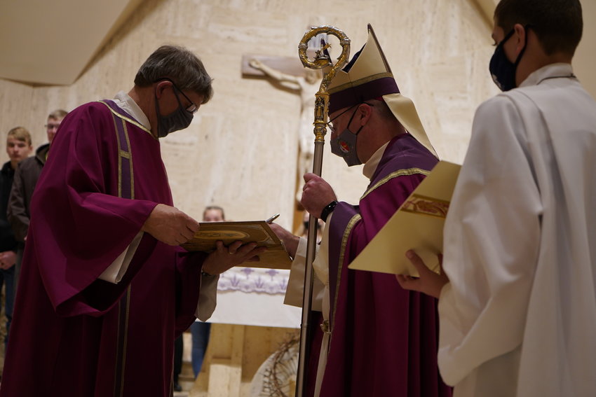 Bishop W. Shawn McKnight signs the Book of the Elect, containing the names of the people who are preparing to receive Baptism in the Catholic Church at the Easter Vigil. Assisting him is Deacon James Haaf of St. Joseph Parish in Westphalia and St. Anthony of Padua Parish in Folk.