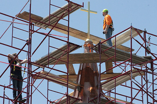 Employees of Renaissance Roofing examine the new cross and copper sheathing on the cupula atop the Cathedral of St. Joseph in Jefferson City April 30. Bishop McKnight blessed the cross before it was lifted into place. Completion on the roof&rsquo;s replacement following last spring&rsquo;s major hail damage will roughly coincide with the bishop&rsquo;s decree restoring the Sunday obligation for the faithful to attend Mass in person.