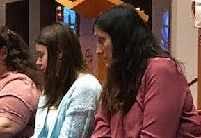 Judith Giger (right) and Karolina (second from right), a foreign exchange student she is hosting in her home this year, who also served as her godmother through the Rite of Christian Initiation of Adults, await having their feet washed during the Mass of the Lord&rsquo;s Supper on Holy Thursday, April 14, in Our Lady of Lourdes Church in Columbia.