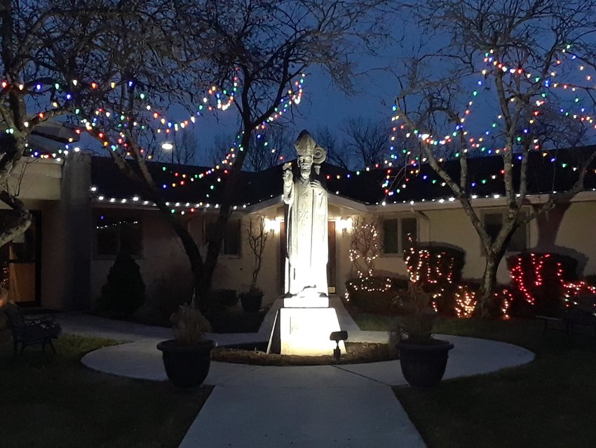 Christmas lights adorn the wedge-shaped garden between St. Patrick Church and the parish rectory in Laurie, where this limestone image of St. Patrick arrived providentially on St. Patrick&rsquo;s Day in 1980.