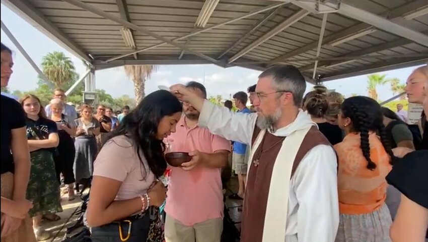 Father Anthony Ariniello, founder of the Community of the Beatitudes, who led the students on pilgrimage and served as their chaplain, renews the pilgrims&rsquo; Baptism while they waited in line for security screening at the Israel-Jordan border, on the way home from their shortened pilgrimage.