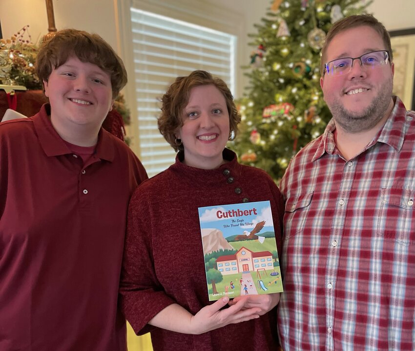 Laura Theissen displays her newly published children&rsquo;s storybook, Cuthbert: The Eagle Who Found His Wings, with her son, Lucas, and her husband, Andy.