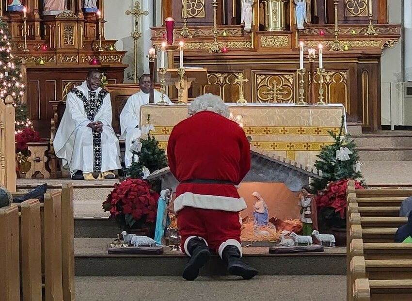 A bearded visitor in red kneels and prays before the Nativity scene in St. Mary of the Angels Church in Wien at the conclusion of Mass on Christmas Eve in this 2022 file photo.