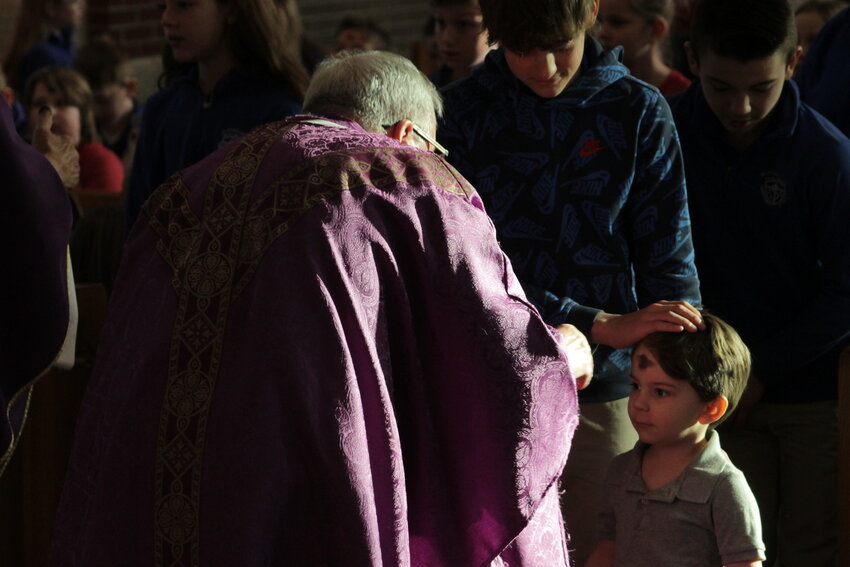 Monsignor David Cox traces ashes in the shape of a cross onto the forehead of a child at an all-school Mass on Ash Wednesday in St. Stanislaus Church in Wardsville.