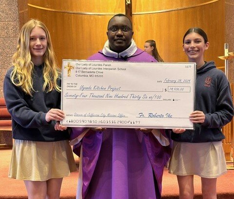 Our Lady of Lourdes Interparish School students present a ceremonial check to Father Simon Kanyike to build a new kitchen for a boarding school in his home archdiocese.