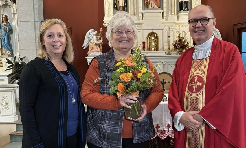 Debbie Reinkemeyer, left, principal of Sacred Heart School in Rich Fountain and Holy Family School in Freeburg, and Father William Debo, pastor of Sacred Heart and Holy Family parishes, present flowers to Linda Neuner on the 50th anniversary of Ms. Neuner joining the Sacred Heart School faculty.