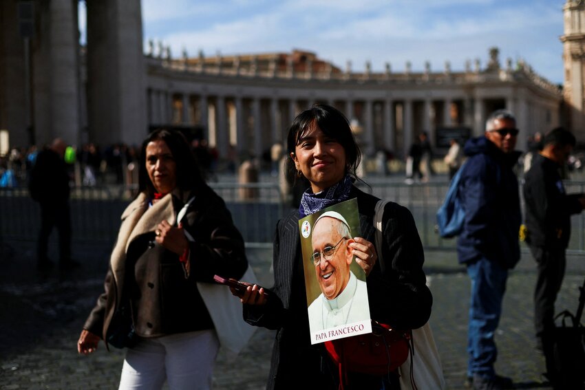 A woman smiles as she holds an image of Pope Francis in St. Peter's Square at the Vatican Feb. 26, 2025, as he continues his treatment for double pneumonia at Rome&rsquo;s Gemelli Hospital