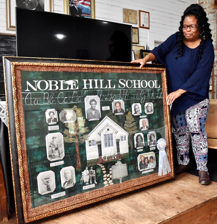 Valerie Coleman, curator of the Noble Hill-Wheeler Memorial Center, positions the framed quilt made by Teresa Cook titled &quot;A Noble Idea Set Upon a Hill&quot; in the venue's main classroom. The quilt was gifted to the center at the 2019 Atlanta Quilt Festival.