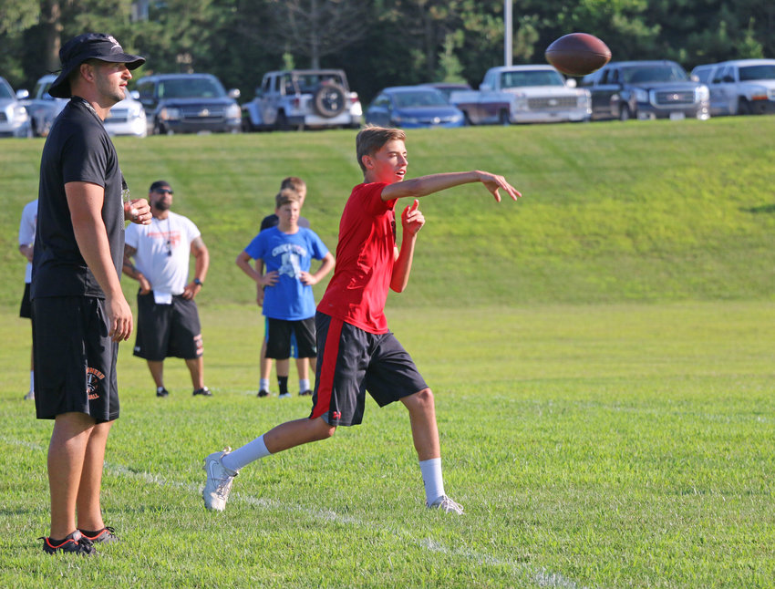 Pioneers football coach Andrew Christensen, left, watches as eighth-grader Austin Welchert throws a pass Wednesday during the Fort Calhoun youth football camp.