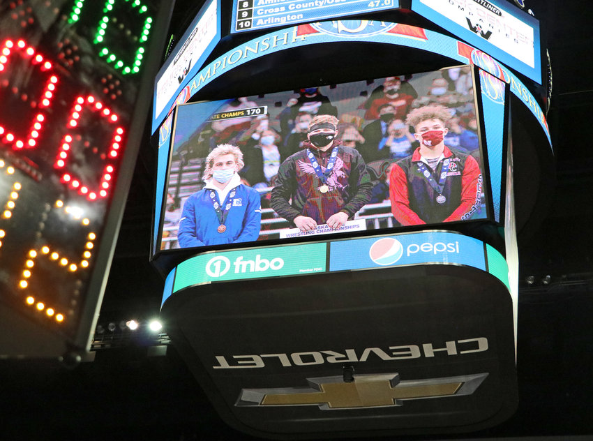 Arlington senior Josh Miller, middle, stands atop the podium with his championship bracket Saturday night on the CHI Health Center scoreboard.
