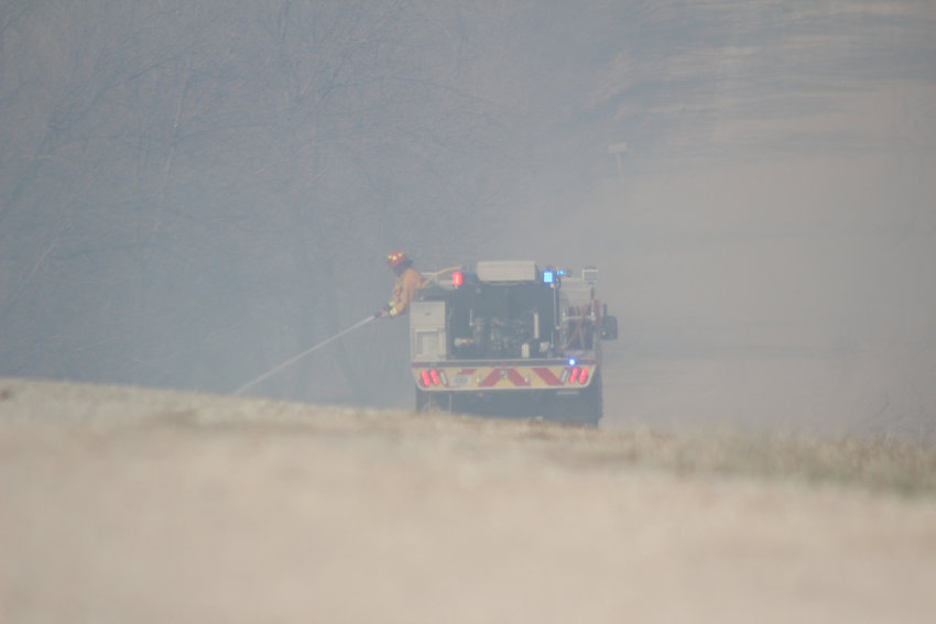 A firefighter sprays water on a field after a barn fire spread Wednesday afternoon.