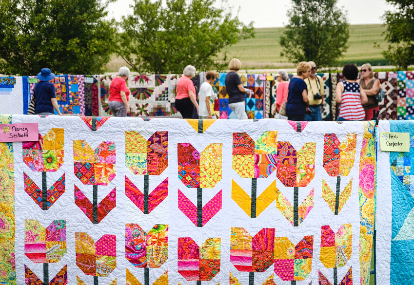 Quilt enthusiasts meet and greet as they walk along rows of quilts displayed on cattle panels during the annual quilt show and garden walk Saturday at Doug and Teri Wolfe's farm.