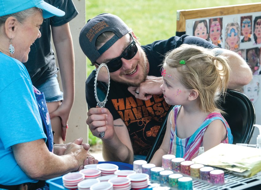 Anthony Blackman holds the mirror so that his daughter, Lorelei, can see her face paint.