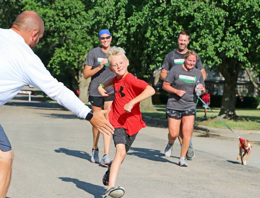 Ryker Nelson, 7, middle, winds up for the finish line high five with Scott Parson on Saturday morning during the Arlington Summer Sizzle celebration.