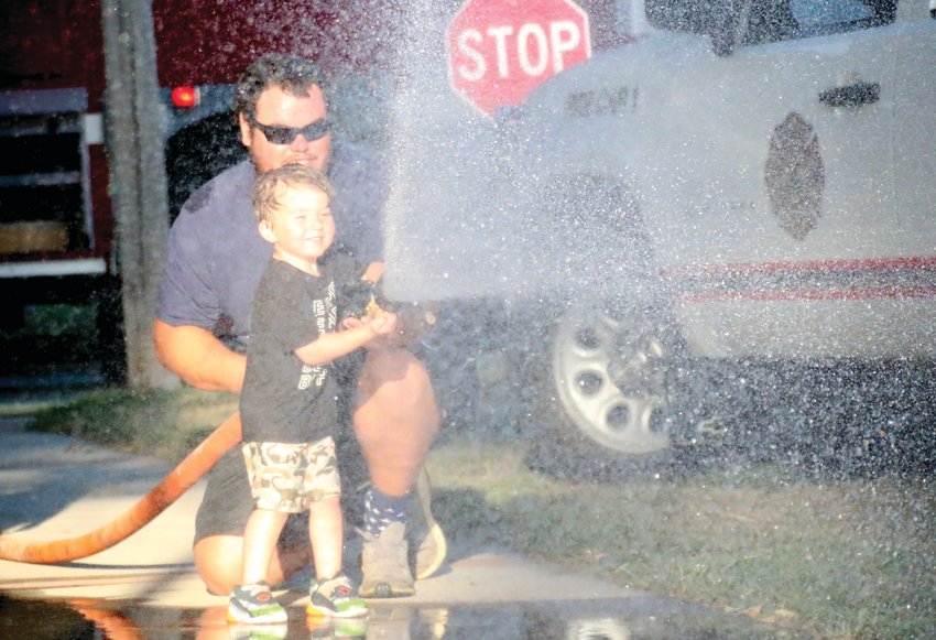Firefighter Blake Gutschow helps Declan Pedersen, 3, shoot a firehose during the Blair Volunteer Fire Department's hydrant party.
