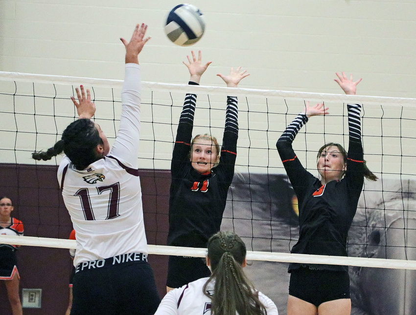 The Eagles' Taylor Arp, left, hits into the block attempt of Olivia Quinlan, middle, and Grace Genoways on Thursday at Arlington High School.