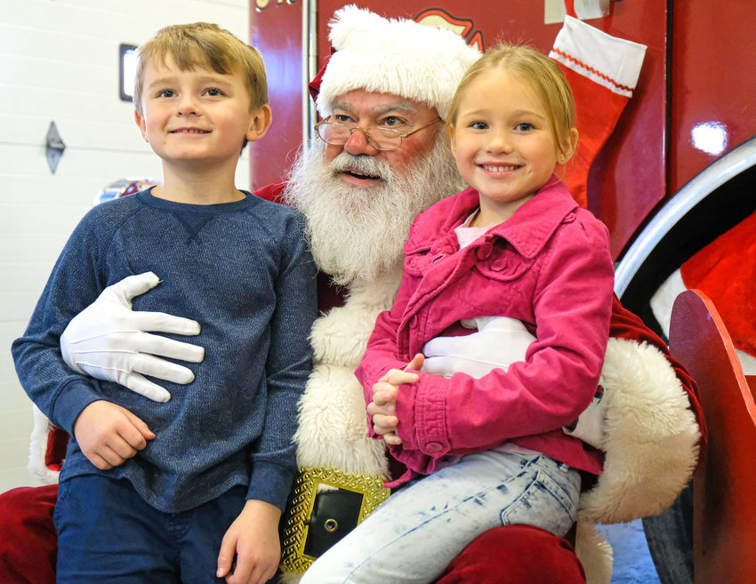 Riley and Morgan Adams sit on Santa&rsquo;s lap to pose for a photo at the Blair South Fire Station during the 2019 visit. This year, due to the pandemic, Santa will greet visitors from the bed of a firetruck.