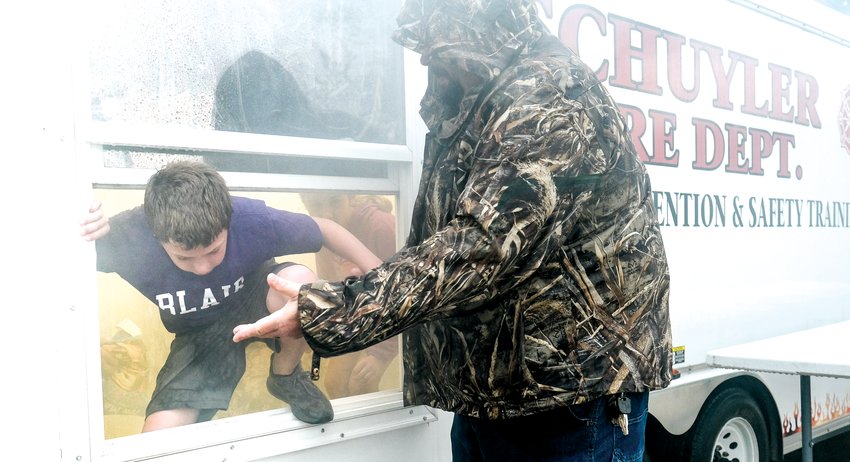 Fire fighter Mike Buttery assists a student in leaving the smoke trailer through an open window at Arbor Park. The smoke trailer helps students practice what to do if they encounter smoke in their homes.