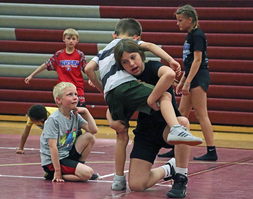 Eighth-grader Brooklyn Ruskamp, middle, facing, demostrates a takedown with Anden Elmore, 7, on Monday during a wrestling camp at Arlington High School.