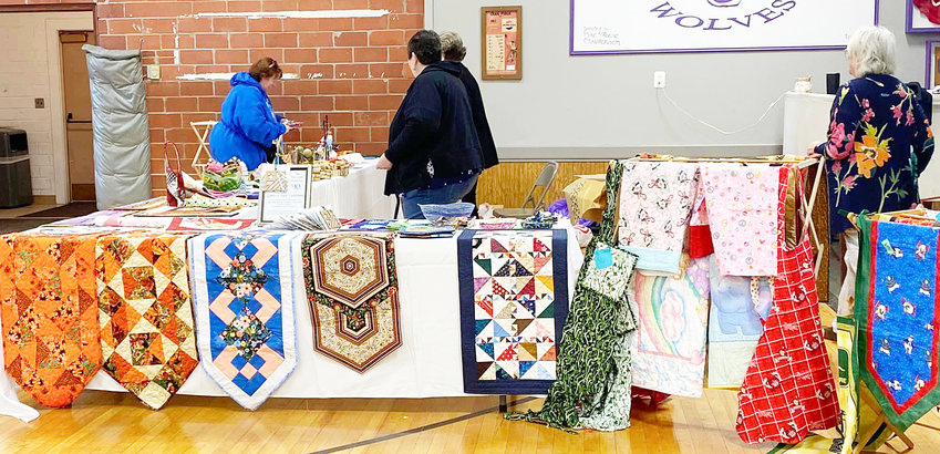Guests look over the quilted creations at the Logan Valley Quilters Guild Bed Turning in the Craig Gym.