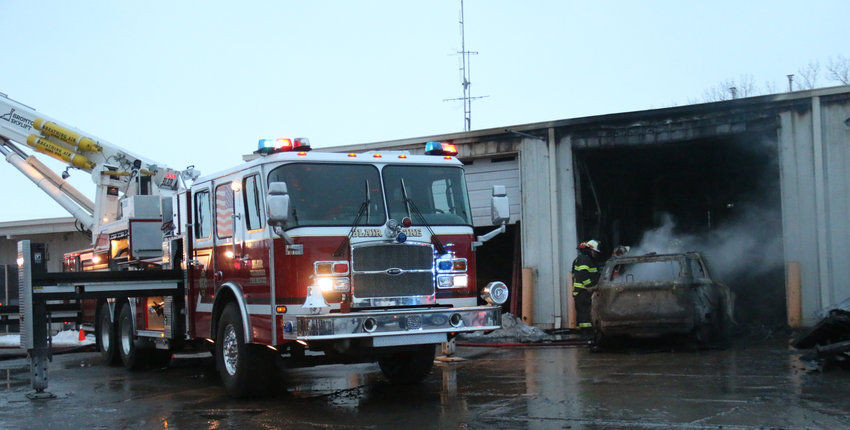 Firefighters manage hotspots at a building on the Woodhouse property following a fire that damaged seven vehicles early Wednesday morning. No one was injured as a result.