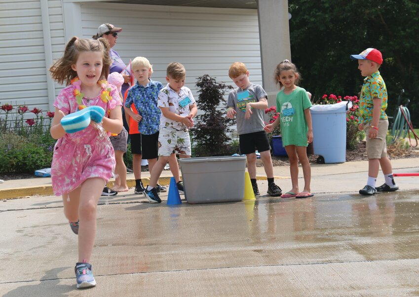 Charlie Ruwe (6) races down the pavement with a sponge to squeeze water into a bucket while playing water-themed games with her group.