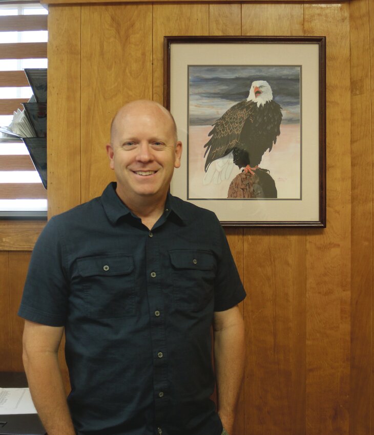 Blair City Treasurer Lindsay Burton stands next to his wife's painting, displayed in his office.