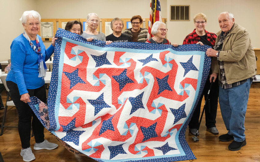 Roland Rasmussen (far right) is this year&rsquo;s recipient of a large patriotic quilt hand crafted by the Blair Bunch quilting group. The the group has been crafting and presenting the quilts to honored veterans for the past ten or more years...