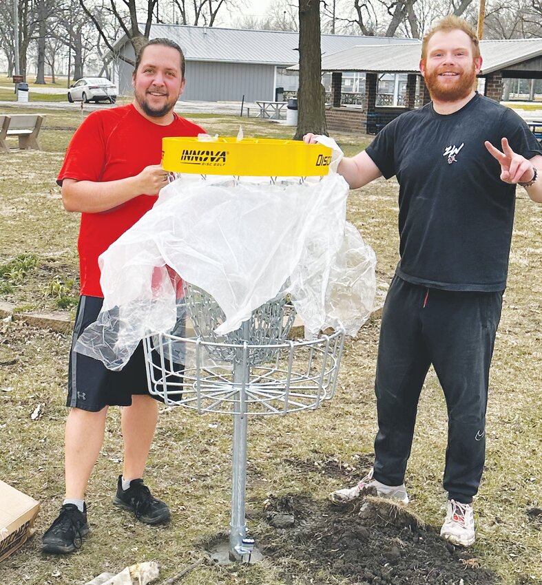 Kyle Watson and Dalton Waterman unwrap  a new disc golf basket in the Oakland Park.