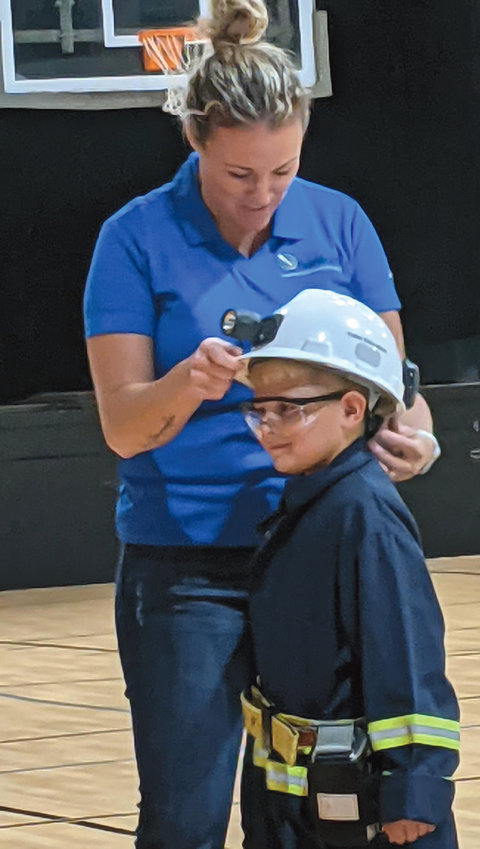 Ashley Armstrong, Science Education Specialist from the Sanford Underground Research Facility in Lead, S.D., presented various topics throughout the day to the students of Iroquois. The youngest students learned how the underground scientists dress and how they get to their workplace underground. Pictured: Ashley Armstrong and first grader, Cason Glanzer, who is dressed as an underground lab scientist.