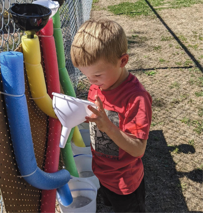 Reed DeJong, preschooler, explores the water funnels in the outdoor classroom.
