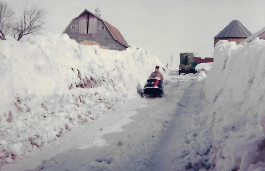 Roy Wade on the snowmobile at the farm driveway. The double corncrib can be seen in front of the barn.&nbsp;