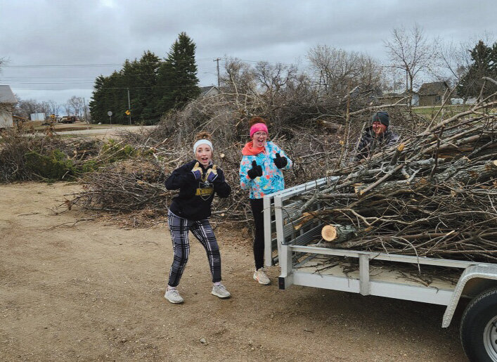 De Smet High School golfers Harper Anderson and Ivey Schoenfelder show their enthusiasm as they help to remove downed branches on the golf course Saturday. Over 30 golfers and Kingsbury County Country Club members volunteered to clean up the damage from earlier storms this winter.