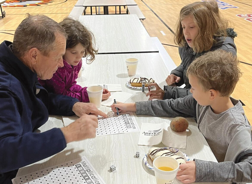 Iroquois Elementary held Digits &amp; Donuts on Wed., Nov. 22 in the school gym. Loved ones were invited to join their students for donuts and math games before school. Eighty students and loved ones attended the event. Kindergartener Ellie Blue, fifth-grader Brianna Blue and second-grader Micah Blue played multiplication squares while eating their donuts with their grandpa Greg Blue during the Donuts &amp; Digits event.