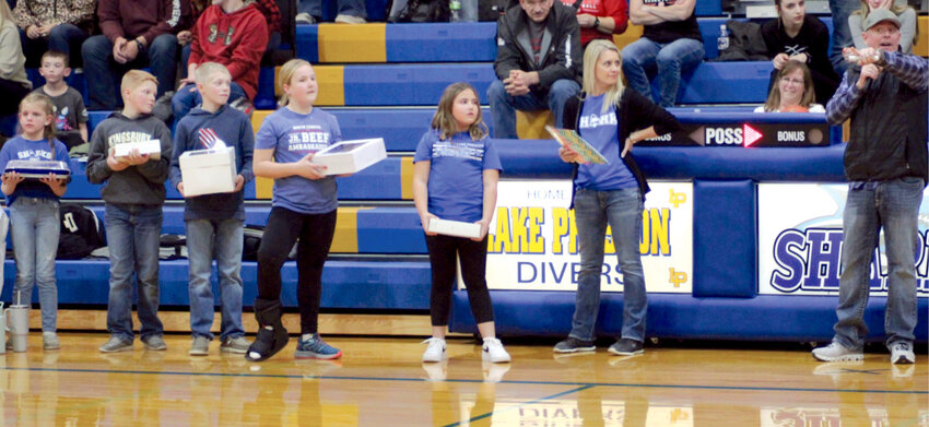 Members of the Busy Blue Bells 4-H Club line up to auction off pies at half-time of the girls basketball game as Ryan Eichler serves as auctioneer.
