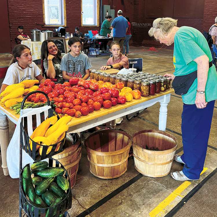 Nancy Holland, volunteer director of the McKenzie Farmers Market, looks at the vegetables and canned items available from Laura Beth Milam and family.