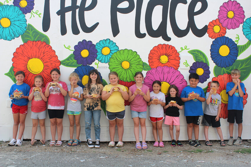 Cooking class students hold their hamburgers in front of the Cedar Street Studio mural. Students included Avery Anderson, Landry Chappell, Maddilyn Chappell, Adeline Johnson, Addie Brown, Anna Kate Tucker, Presley Shipp, Merritt Ghyers, Avery Cooper, Cason Hernandez, Hunter Johnson, and Colin Yeley.
