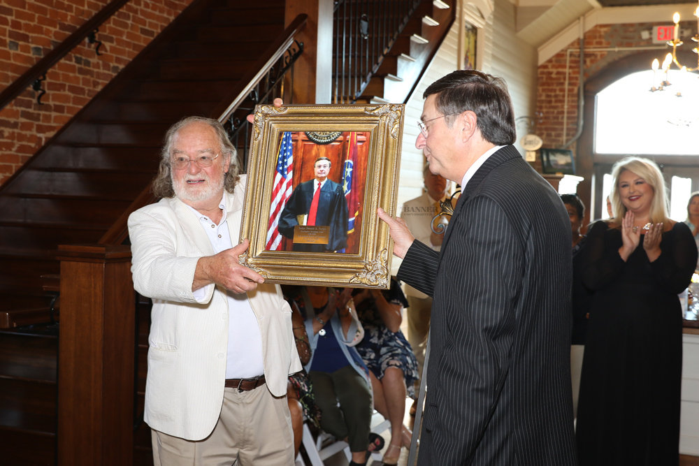 Steve West and Donald Parish unveil a portrait of Donald Parish that will be displayed in the Carroll County Courthouse. In the background is Caroline Parish.