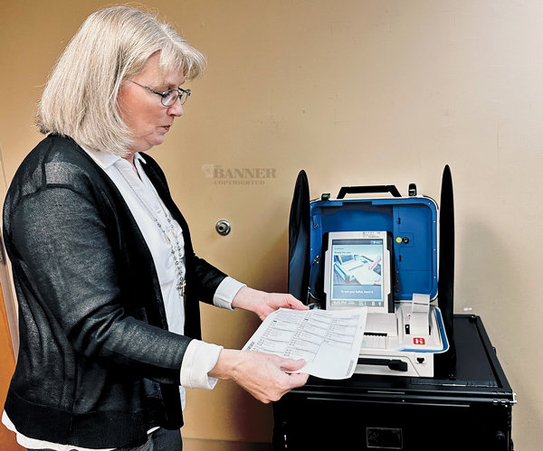 Peg Hamlett demonstrates how a paper ballot is placed in the scanner to record the vote.