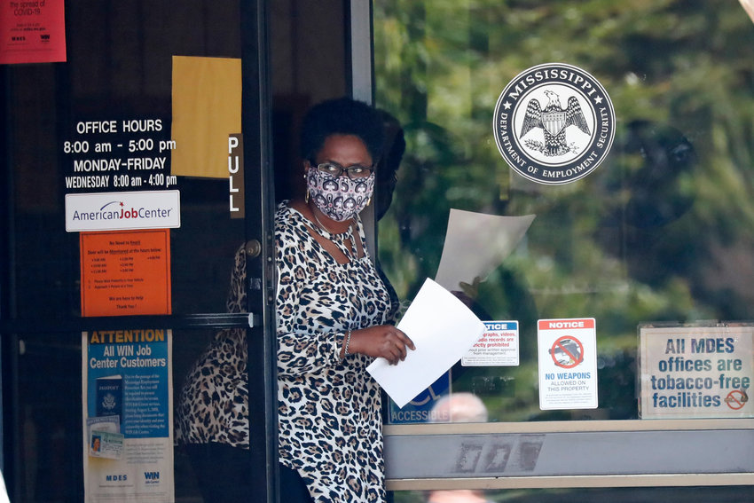 A masked worker at this state WIN job center in Pearl, Miss., holds an unemployment benefit application form as she waits for a client, Tuesday, April 21, 2020. The job centers lobbies are closed statewide to prevent the spread of COVID-19. However the continuing growth of unemployment demands and now additional assistance for self-employed, church employees, gig workers, and others who were previously ineligible for unemployment assistance has drawn some people to the centers for information and to obtain and submit unemployment benefit applications. (AP Photo/Rogelio V. Solis)