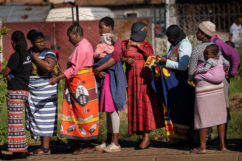 FILE- In this file photo taken Thursday, April 30, 2020, Women carrying their children lineup to receive vegetables from the Jan Hofmeyer community services in the Vrededorp neighborhood of Johannesburg. South Africa is struggling to balance its fight against the coronavirus with its dire need to resume economic activity. The country with the Africa&rsquo;s most developed economy also has its highest number of infections &mdash; more than 19,000.  (AP Photo/Jerome Delay, file)