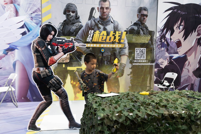 A child plays with a toy gun during a promotion for online games in Beijing on Saturday, Aug. 29, 2020. China is banning children from playing online games for more than three hours a week, the harshest restriction so far on the game industry as Chinese regulators continue cracking down on the technology sector. (AP Photo/Ng Han Guan)