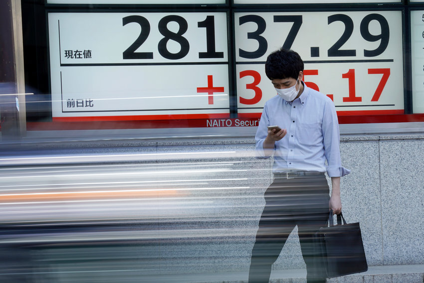 A man wearing a protective mask rides a bicycle in front of an electronic stock board showing Japan's Nikkei 225 index at a securities firm Wednesday, Oct. 6, 2021, in Tokyo. (AP Photo/Eugene Hoshiko)