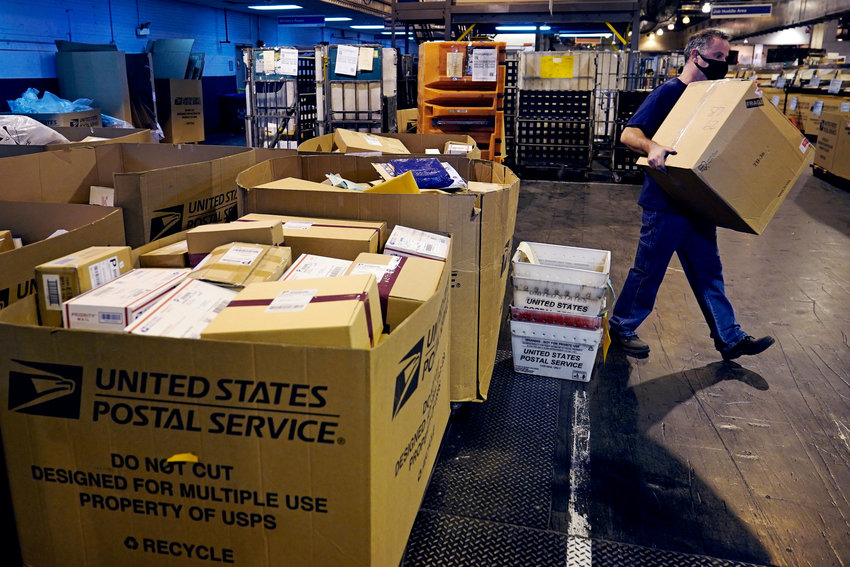 A worker carries a large parcel at the United States Postal Service sorting and processing facility, Thursday, Nov. 18, 2021, in Boston. Last year's holiday season was far from the most wonderful time of the year for the beleaguered U.S. Postal Service. Shippers are now gearing up for another holiday crush.(AP Photo/Charles Krupa)