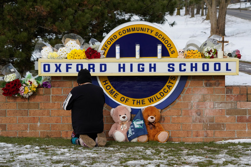 A well wisher kneels to pray at a memorial on the sign of Oxford High School in Oxford, Mich., Wednesday, Dec. 1, 2021. Authorities say a 15-year-old sophomore opened fire at Oxford High School, killing three students and wounding eight other people, including a teacher on Tuesday. (AP Photo/Paul Sancya)