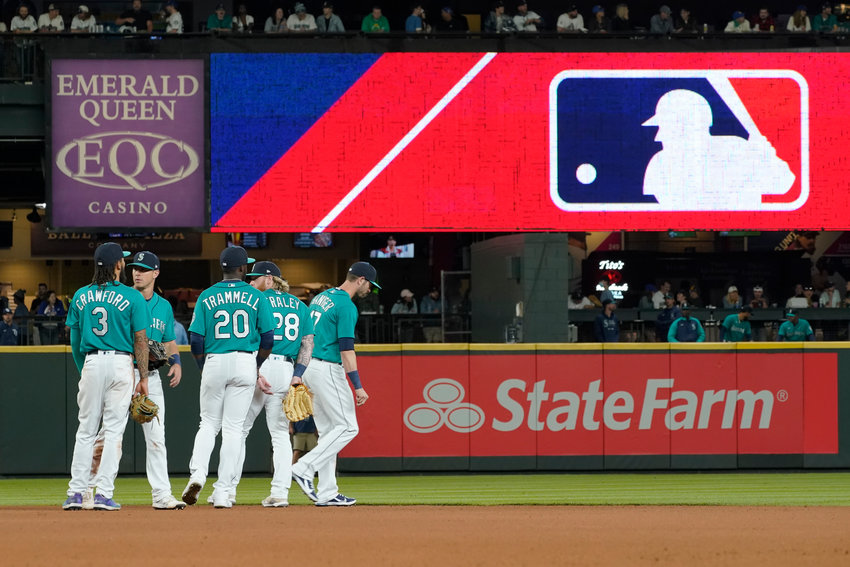 FILE - Seattle Mariners gather as the MLB logo is shown during a review of an attempted catch by right fielder Mitch Haniger of a ball hit by Tampa Bay Rays' Ji-Man Choi that was originally called an out during the ninth inning of a baseball game Friday, June 18, 2021, in Seattle. The call was overturned. The Mariners won 5-1. The clock ticked down toward the expiration of Major League Baseball&rsquo;s collective bargaining agreement at 11:59 p.m. EST Wednesday night, Dec. 1, 2021, and what was likely to be a management lockout ending the sport&rsquo;s labor peace at over 26 1/2 years. (AP Photo/Ted S. Warren)
